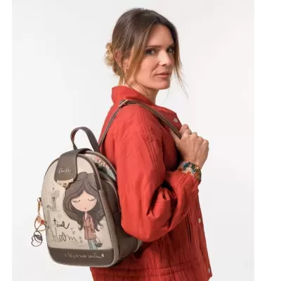 Mochila pequena castanha e bege com ilustração de rapariga e texto TIME TO BLOOM, usada por mulher com casaco vermelho