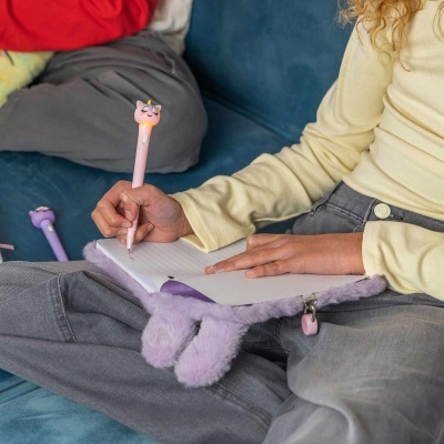 Caneta rosa com cabeça de unicórnio e caderno com capa peluda lilás.