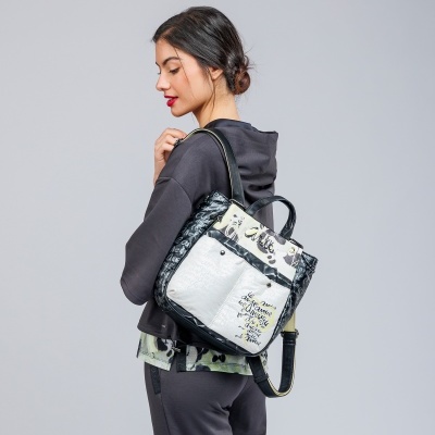 Mochila quadrada preta e branca com texto, alças pretas e prateadas, mulher de perfil a usar