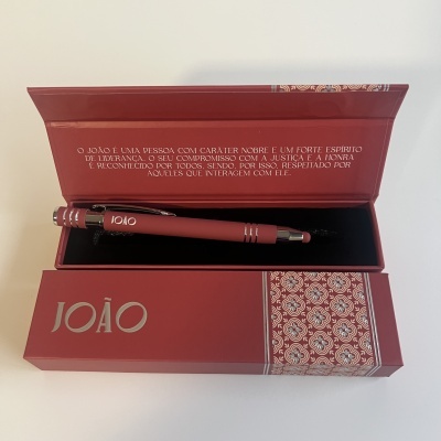 Caneta vermelha dentro de caixa vermelha com tampa aberta e texto decorativo