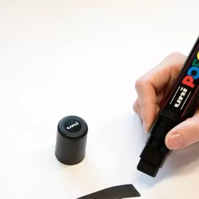 Marcador permanente preto POSCA com tampa retirada e mão a desenhar