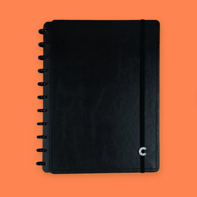 Caderno preto com capa rígida, argolas e elástico, fundo laranja.