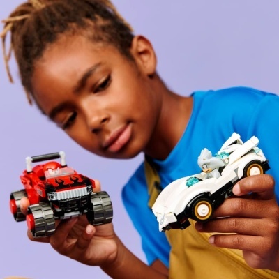 Criança a segurar dois carros de brinquedo, vermelho com chamas e branco com personagem