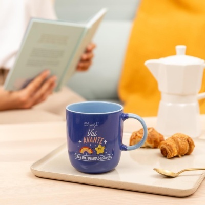 Caneca azul com texto motivacional e desenhos numa bandeja com croissants e colher