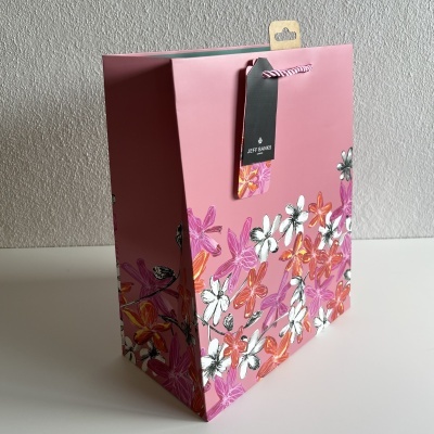 Saco de papel rosa com flores coloridas e etiqueta preta pendurada