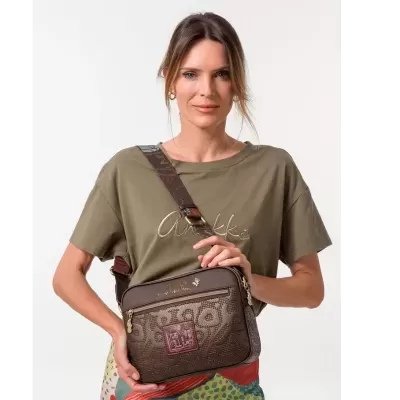 Mulher a segurar mala castanha com padrão e t-shirt verde oliva com texto