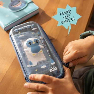 Estojo azul transparente com desenho de pinguim em mesa de madeira com mãos a abrir o fecho