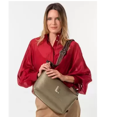 Mulher com blusa vermelha e calças castanhas segurando uma sacola verde com alça castanha larga.