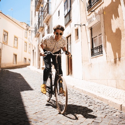 Homem jovem de bicicleta num passeio urbano com camisa floral e sapatilhas amarelas