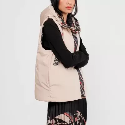 Colete acolchoado bege com capuz e padrão interior, usado com blusa preta e saia estampada