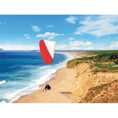 Parapente vermelho e branco sobre praia com falésias e mar azul