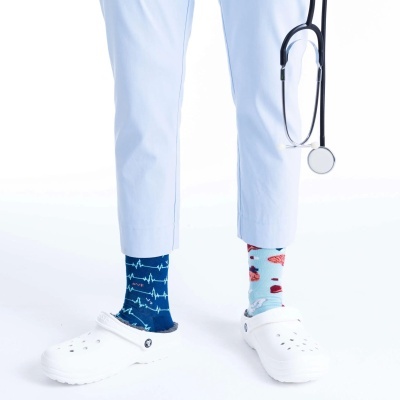 Meias coloridas com padrões médicos, calçado branco tipo Crocs, calças brancas e estetoscópio.