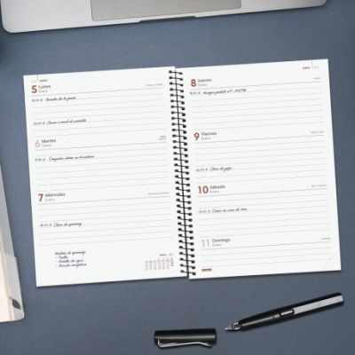 Agenda semanal aberta com anotações manuscritas e caneta preta sobre superfície cinzenta