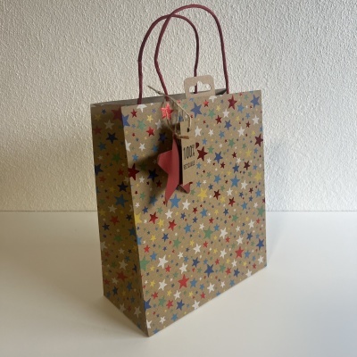 Saco de papel castanho com estrelas coloridas e alças vermelhas