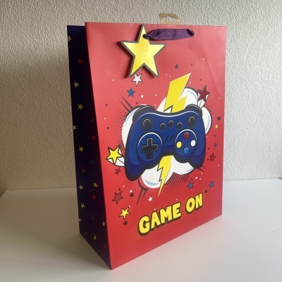 Saco de presente vermelho com desenho de comando de videojogo azul e texto GAME ON
