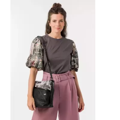 Mulher com t-shirt cinza de mangas estampadas e calças rosa, segurando mala preta com padrão igual às mangas