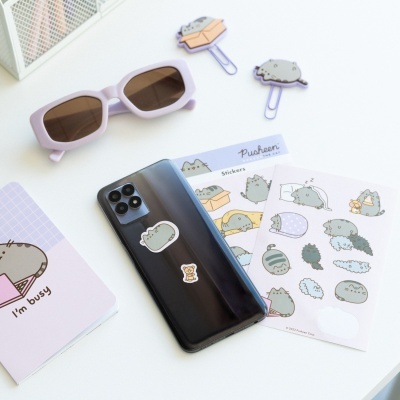 Smartphone preto com autocolantes Pusheen e acessórios Pusheen numa mesa