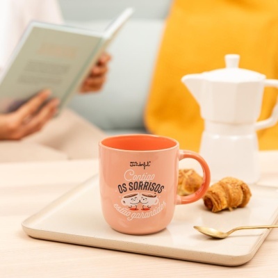 Caneca cor de salmão com texto, mini-croissants, colher dourada, cafeteira branca e almofada amarela