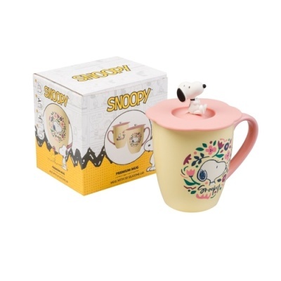 Caneca amarela com tampa rosa e figura do Snoopy, ao lado caixa temática