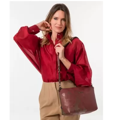 Mulher com blusa vermelha, calças bege e mala bordô de ombro com padrão abstrato