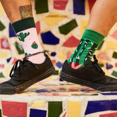 Meias coloridas com desenhos de cactos usadas com sapatos pretos e fundo de azulejos multicoloridos