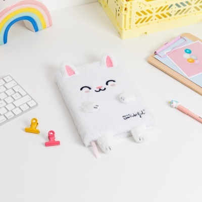 Caderno felpudo branco com desenho de gato e texto bordado numa mesa com acessórios de escritório coloridos