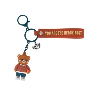 Porta-chaves com urso castanho com bola, fita laranja com texto e pendente branco.