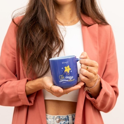 Caneca azul com estrela amarela e texto Tio, contigo é tudo mais divertido! segurada por uma mulher com casaco rosa.