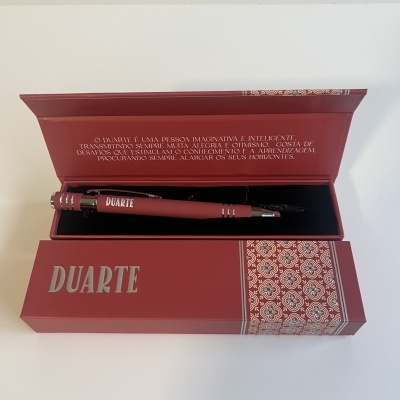 Estojo vermelho com caneta preta 'DUARTE' e texto em português no interior da tampa