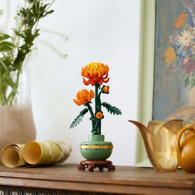 Miniatura de flores de LEGO cor de laranja num vaso verde sobre mesa de madeira ao lado de jarro âmbar.