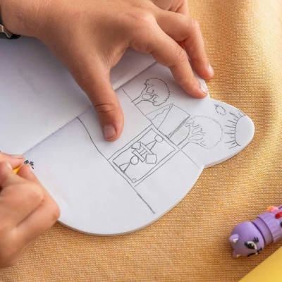 Pessoa a desenhar num caderno em forma de rato com desenhos a lápis