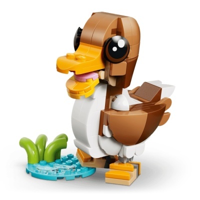 Figura de pato feita com peças de construção coloridas em branco, castanho, amarelo e preto com base azul e plantas verdes.