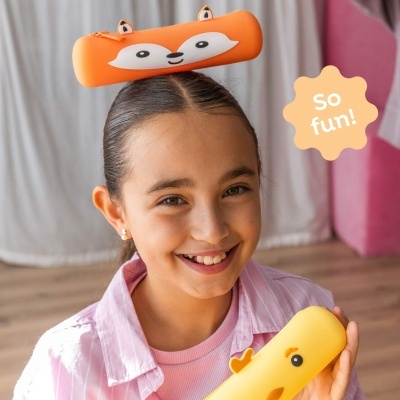 Criança sorridente com estojo escolar laranja com olhos e orelhas na cabeça e estojo amarelo com olhos na mão