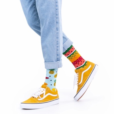 Meias coloridas com padrão de frutas tropicais e ténis amarelos com sola branca, em fundo branco