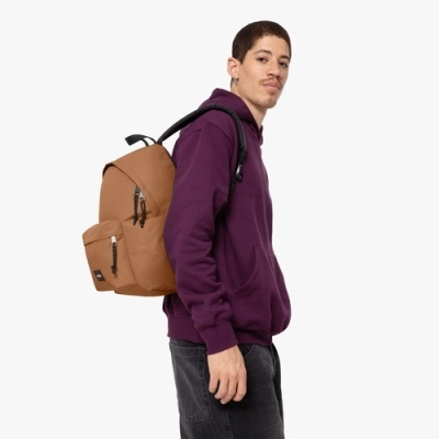 Mochila castanha em tecido com bolso frontal e fechos, usada por homem com hoodie roxo.