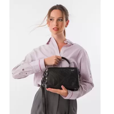 Mulher segurando mala preta Anekke com camisa rosa e calças cinzentas