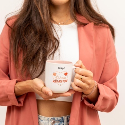 Mulher segurando caneca branca com interior rosa e texto em vermelho