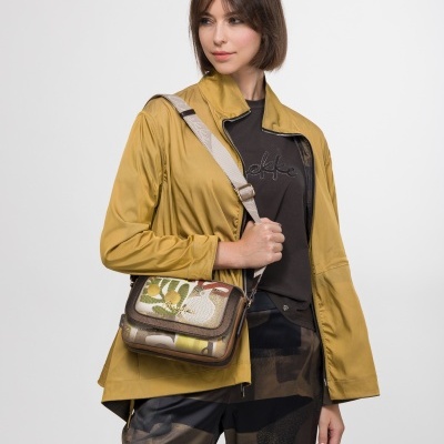 Mulher com jaqueta amarela, t-shirt preta com texto 'Anekke', calças estampadas e mala colorida com alça bege