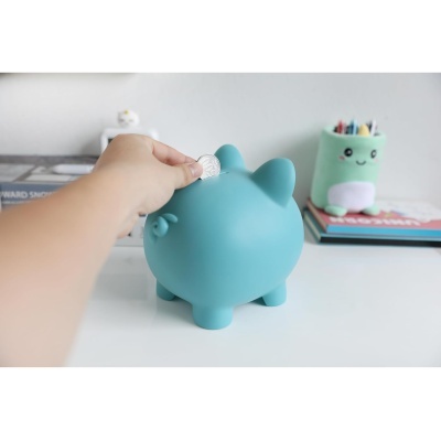 Mão a colocar uma moeda numa poupança em forma de porco azul sobre uma mesa branca