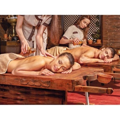 Duas pessoas a receber massagem com óleo em camas de madeira em spa