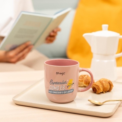 Caneca rosa com texto motivacional em cima de bandeja branca com croissants e colher sobre mesa clara