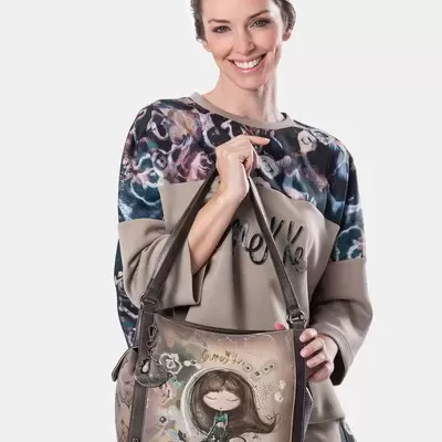 Mulher a segurar mala bege com desenho de rapariga, veste roupa bege com padrão colorido