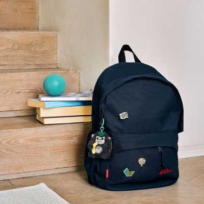 Mochila preta com pins coloridos e pendente peludo junto a escada em madeira e livros.