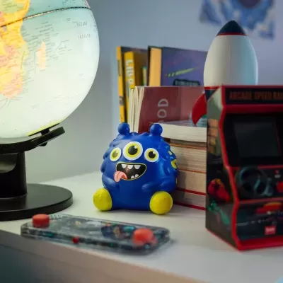 Globo iluminado, brinquedo azul de personagem com três olhos, foguete e mini arcade em cima de uma mesa.