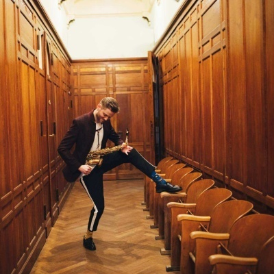 Homem com saxofone num corredor de madeira com bancos