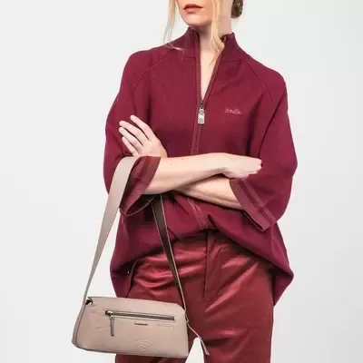 Mulher com camisola vinho e calças vermelhas segurando mala bege de pele