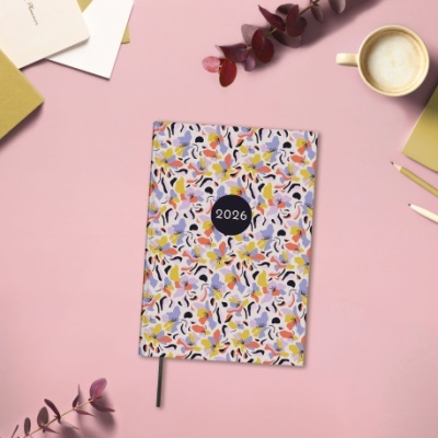 Agenda 2026 colorida sobre mesa rosa com café, canetas e folhas decorativas