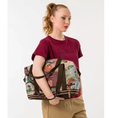 Mala de mão colorida com padrão floral e alças castanhas, usada por mulher com t-shirt vinho e calças bege