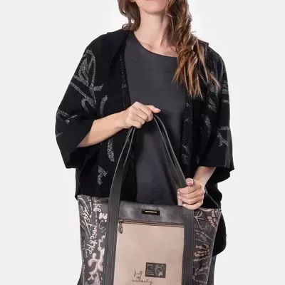 Mulher com blusa preta e casaco com padrão cinza a segurar mala tote bege e preta com bolso frontal