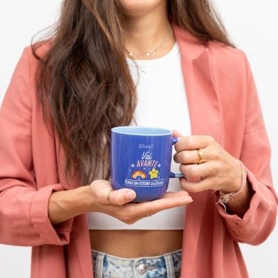 Caneca azul com texto e ilustrações a ser segurada por mulher de casaco rosa